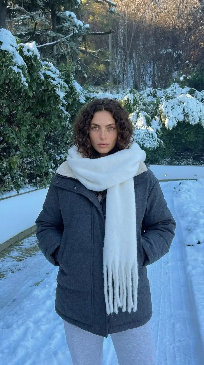 Vertical winter portrait with snow-covered greenery background and layered cold-weather clothing.